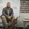 Joseph Curry sitting and posing in front of his classroom.