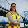 Honoree Maria Drawbaugh wearing a yellow workvest and standing in front of a bridge