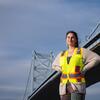 Honoree Maria Drawbaugh standing in front of a bridge and wearing a yellow vest