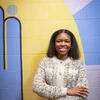 Honoree Sydney Smith smiling and leaning against a mural at the elementary school where she teaches